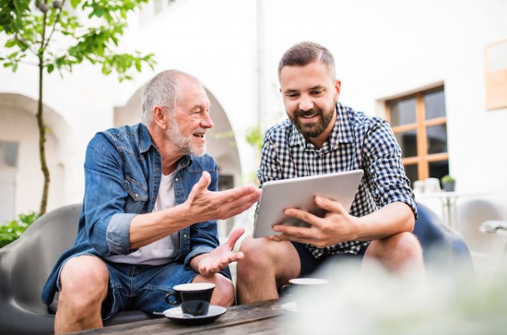 young man teaching a old man using tablet