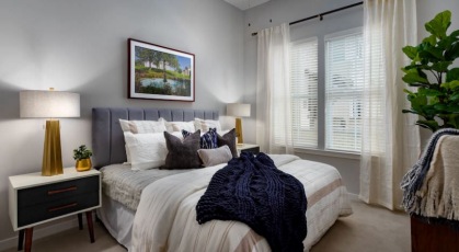 Model bedroom at our 55 and over community in Henrico, VA, featuring carpeted flooring and windows with blinds.