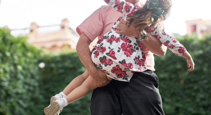 grandfather carrying his granddaughter with her arms outstretched in park