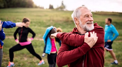 elderly man stretches with his family in the background getting ready to work out in the park