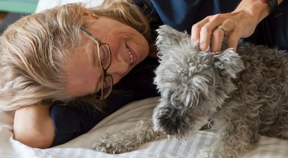 older woman laying on bed, petting her dog
