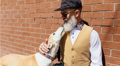 man with a white beard pets dog who's looking up at him