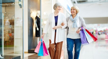 friends walk arm in arm through shopping center with shopping bags