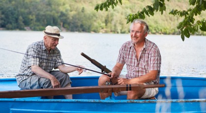 father and son sit in row boat fishing on lake