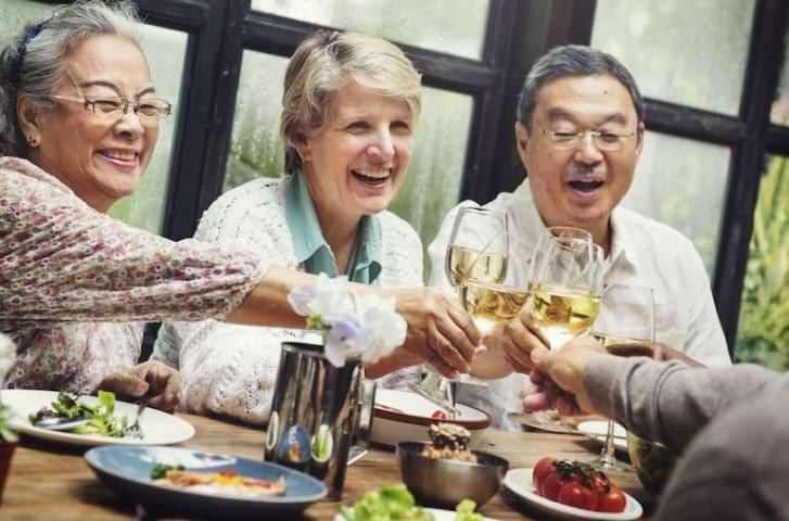 Group of happy senior friends cheering at meal